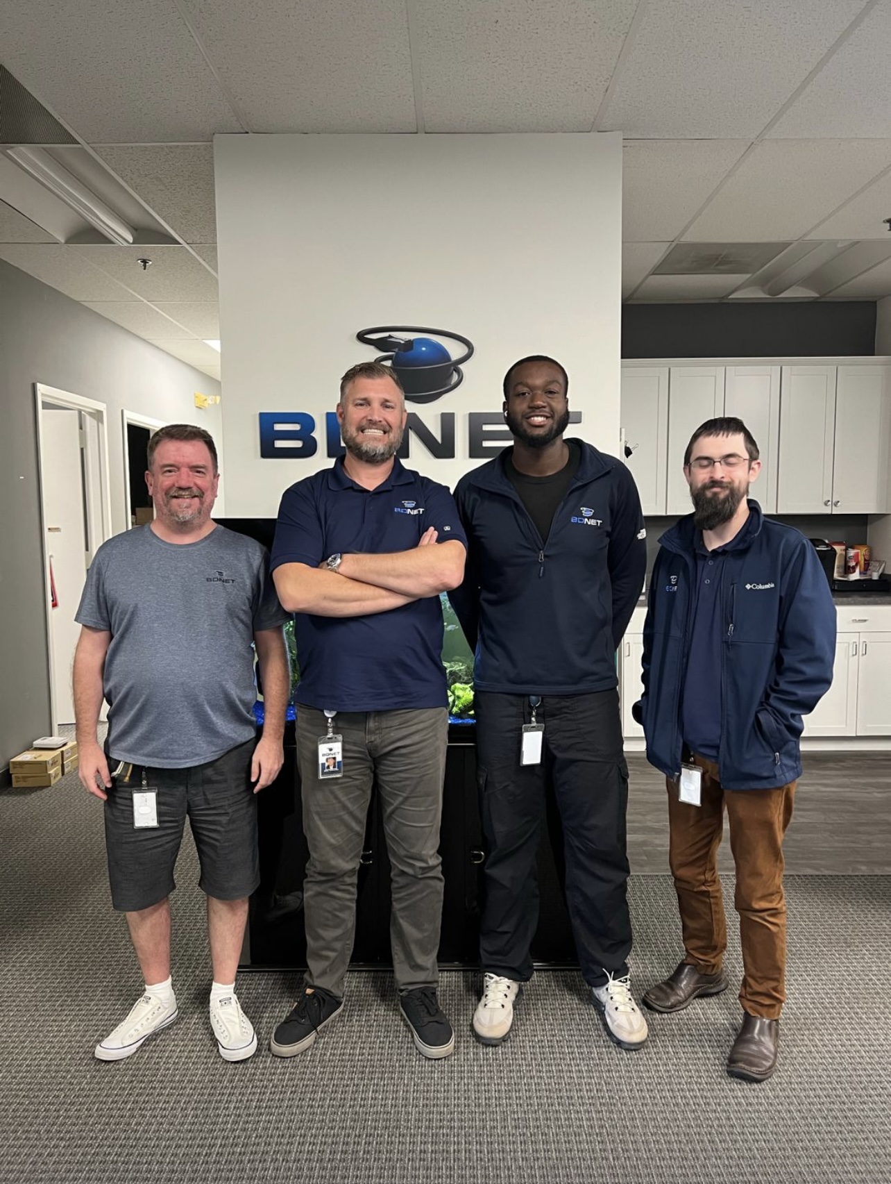 Four men standing in an office in front of a sign that reads "BDNET."

