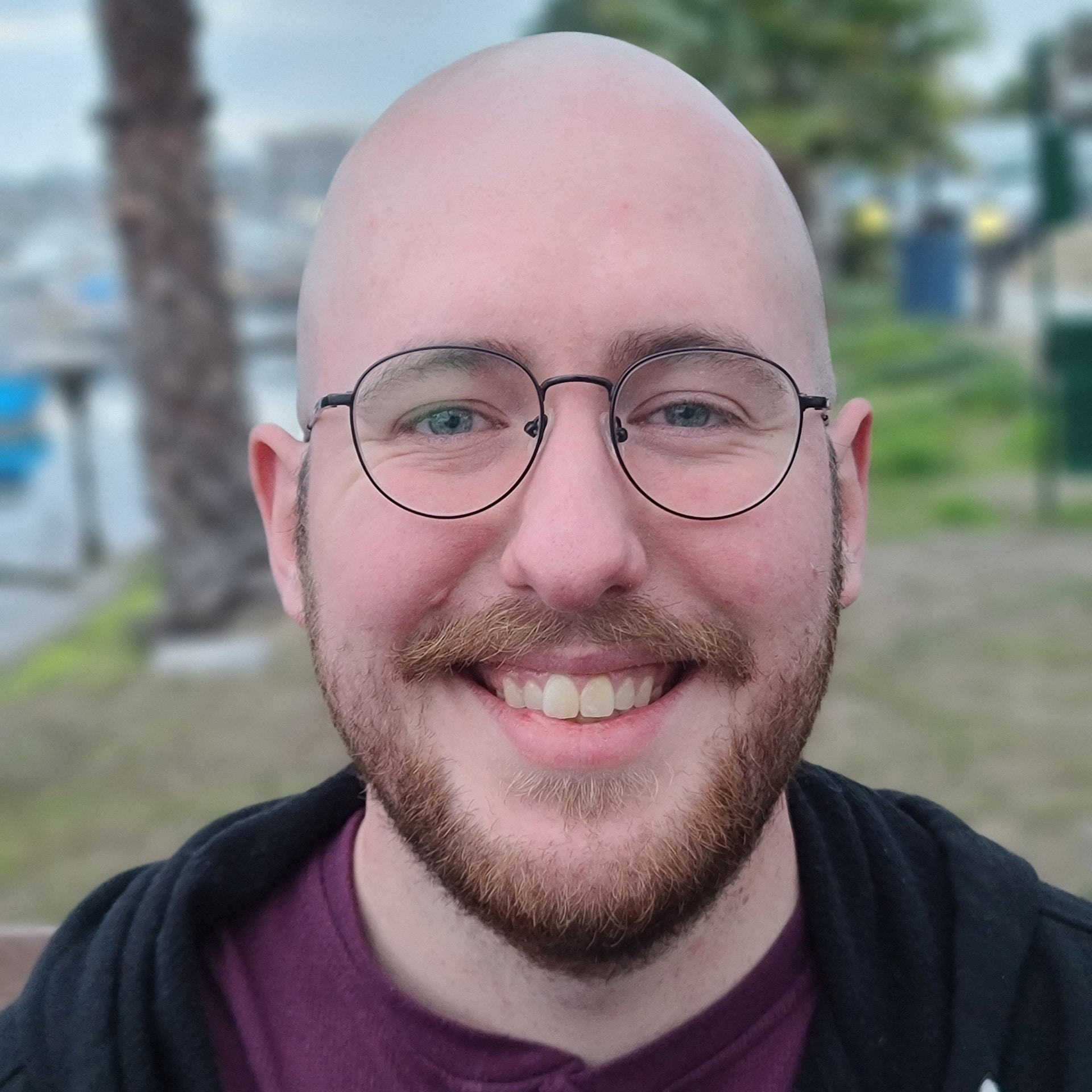 A bespectacled, bald man in his late twenties smiles at the camera.